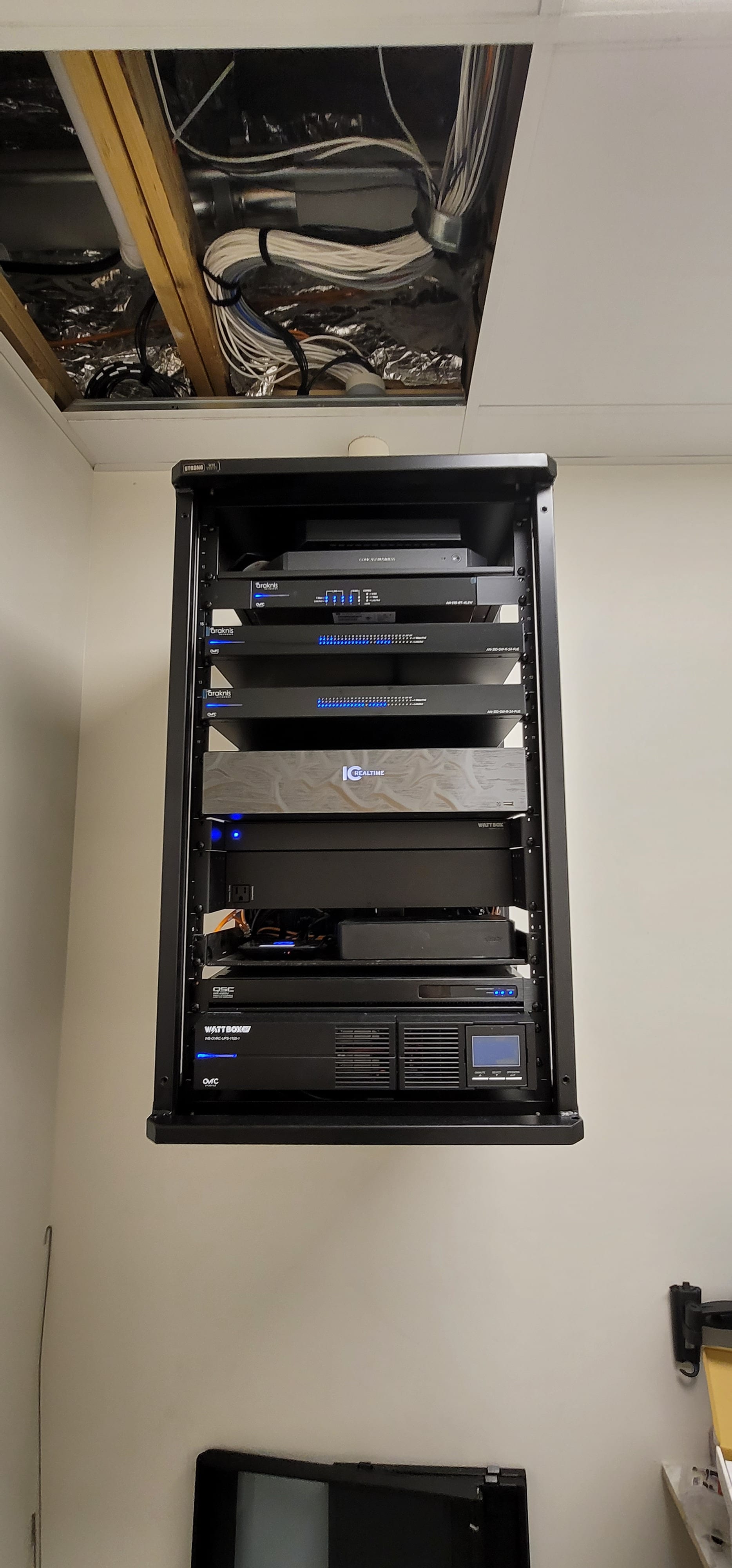 Pristine custom AV equipment rack with rack-mounted amplifiers, processors, and managed network gear, blue indicator LEDs across the front