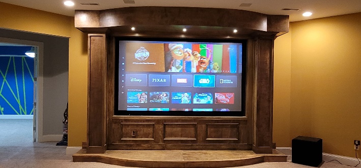 Finished Noble A-V home theater - wood-arched proscenium with acoustic-transparent screen lit, matching the install in progress on the left